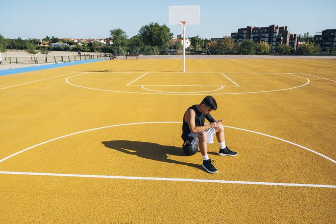 Male basketball player using his smartphone resting after training