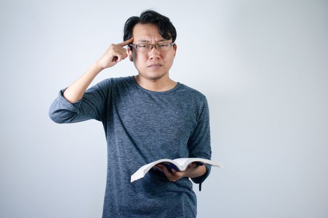Asian young male reading book with thinking gesture