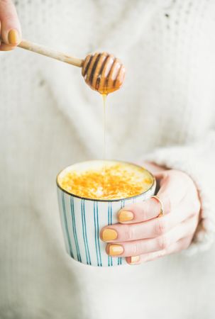 Female using honey dipper to add honey to latte