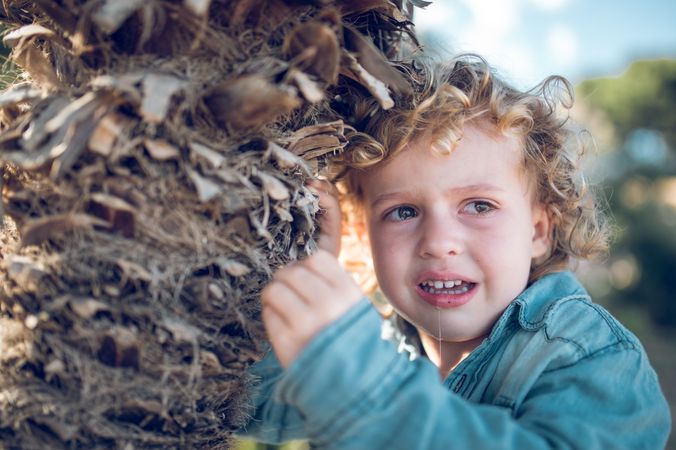 Crying boy near tree trunk