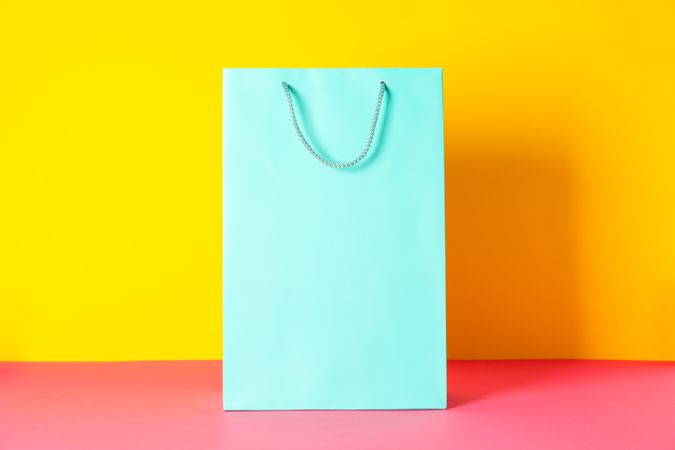 Color paper bag on pink table against yellow background, copy space