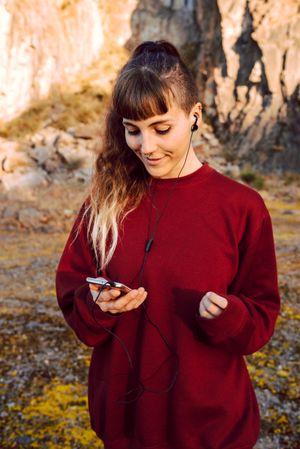 Young woman with piercing listening music on smartphone on hill
