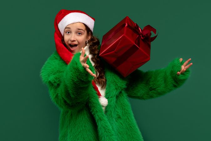 Girl in Santa hat and fur coat tossing gift.