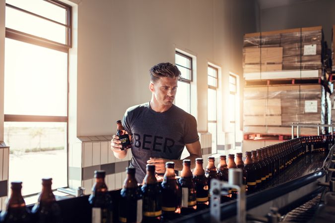 Young man working at small craft beer making factory and checking quality of alcoholic beverages