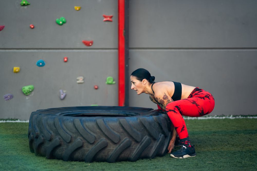 Side view of fit woman lifting a truck wheel in a gym