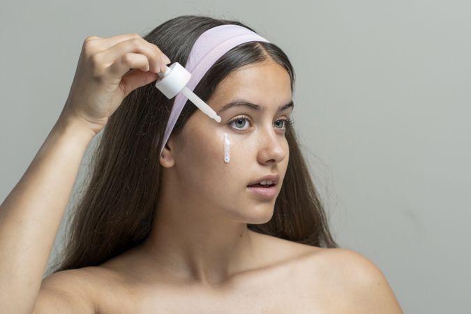 Young woman applying a milky eye serum or hydrating essence from a dropper