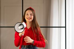 Teen girl smiling holding megaphone in bright indoor setting.
