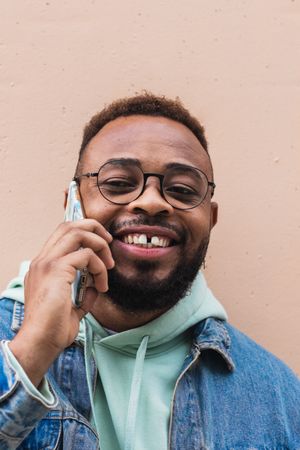 Cheerful Black man talking on phone near wall