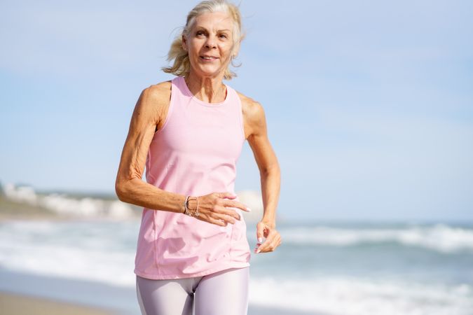 Older woman in sports wear jogging along beach