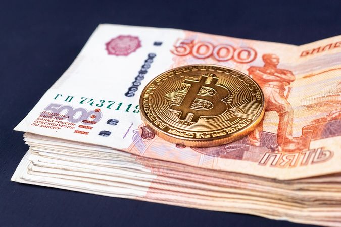 Bitcoin on a stack of 5000 Russian ruble on a table