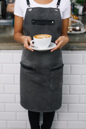Barista in apron holding large cappuccino, vertical