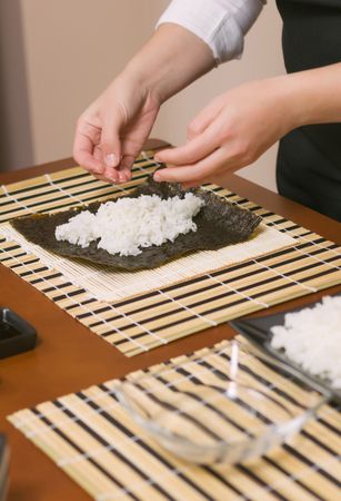 Hands of chef preparing rice in sushi rolls