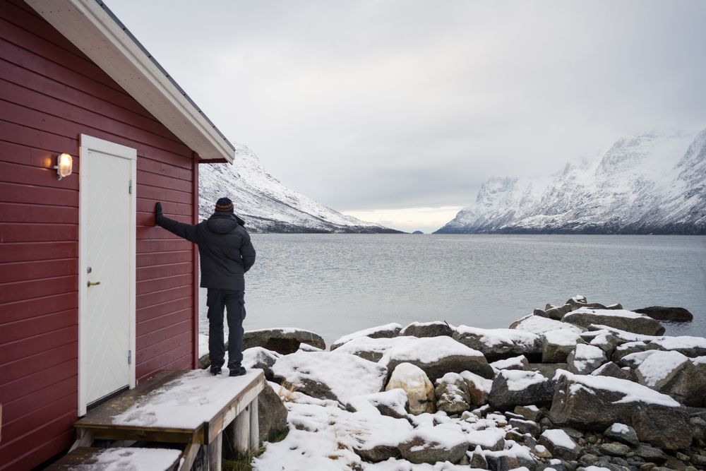 Solitary man on rocky shore against tranquil lake and snowy mountains in cold day