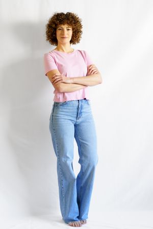 Woman in pink t-shirt and jeans standing barefoot in bright studio