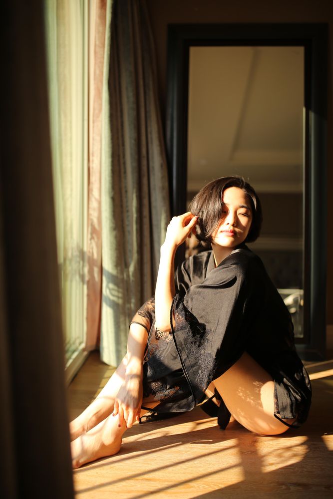 Woman in dark top and shorts sitting on wooden floor beside window