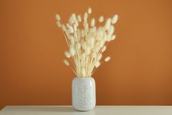Vase of dried bunny tail bouquet centered on table in brown room