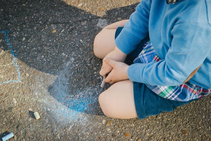Child sitting on asphalt with colorful chalks