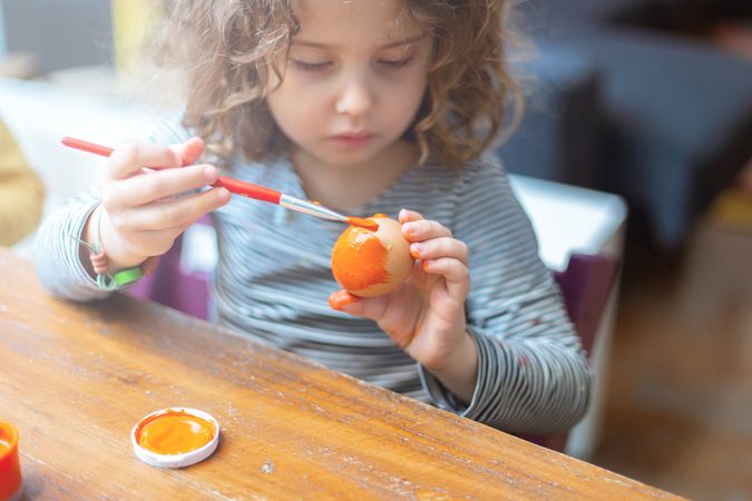 Toddler girl painting egg at table