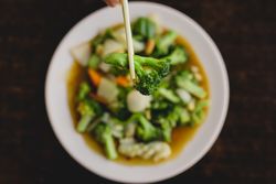 Hand holding broccoli with chopsticks over vegetarian soup