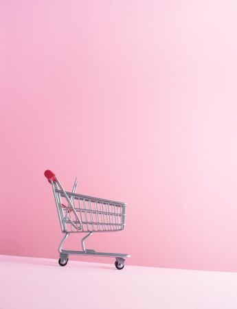 Shopping cart rolling downward over pink background