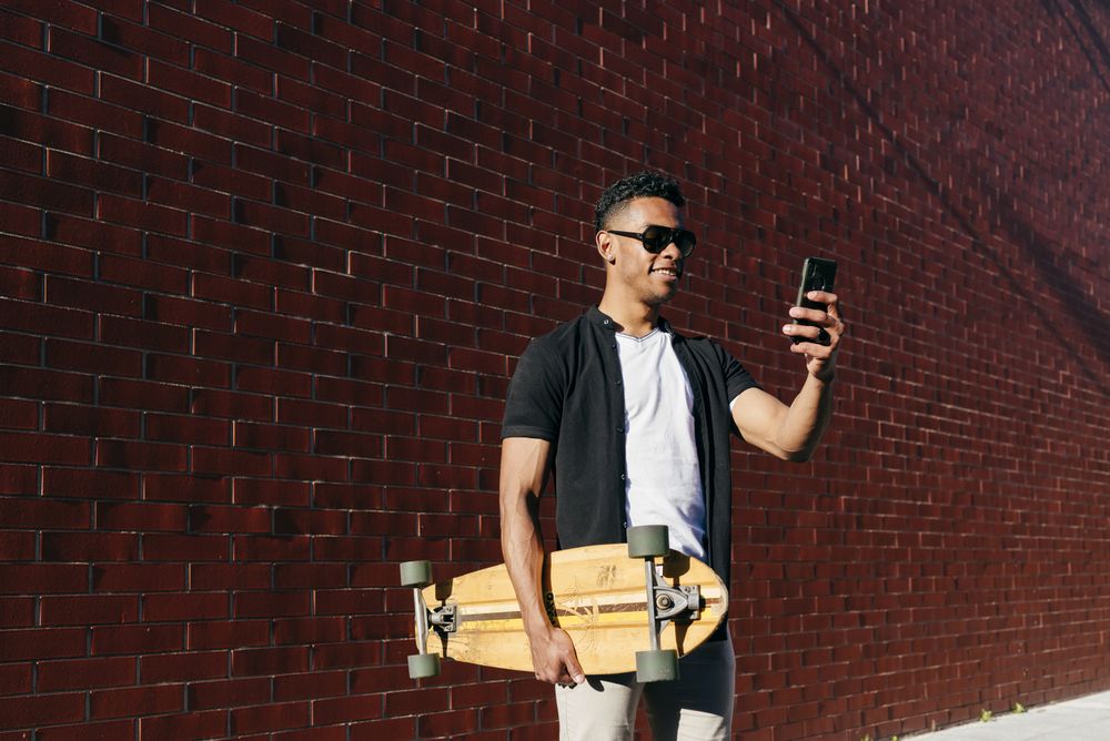 Young Black male with long board speaking on phone