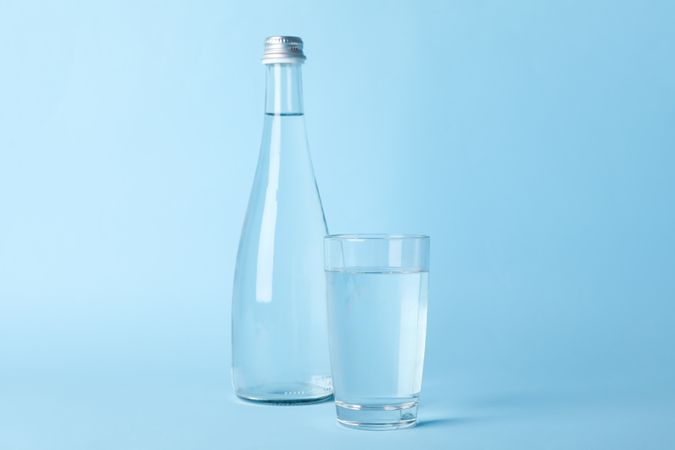 Water bottle with glass full of water in light blue room