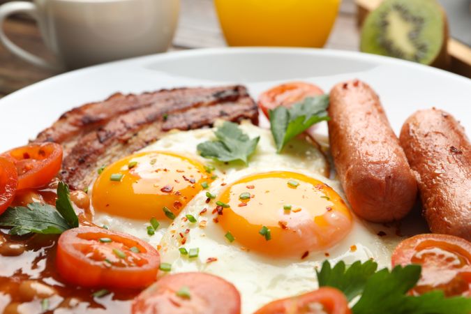 Two fried eggs sunny side up on plate with bacon and sausage