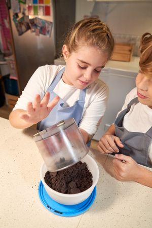 Siblings pouring crashed cookies into bowl