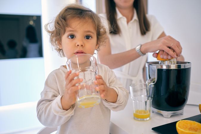 Cute boy drinking glass of orange juice in kitchen