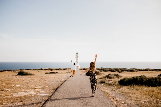Happy lovers jumping with arms raised on path to lighthouse