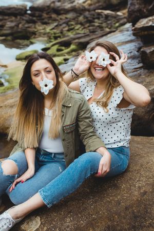 Young female travelers sitting on stone and covering eyes with flowers
