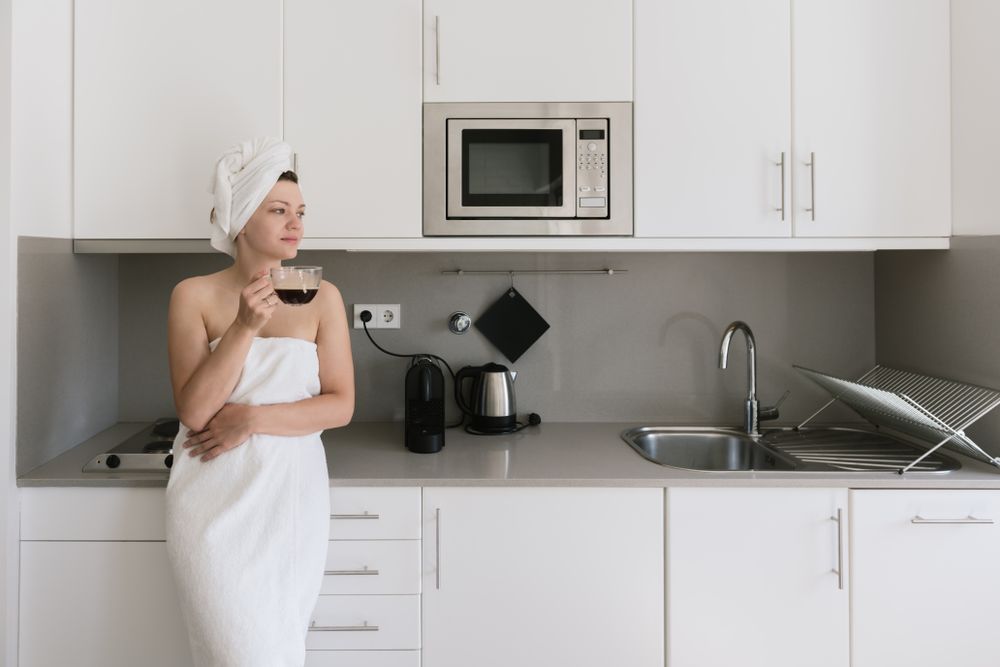 Joyful adult woman enjoying day off while having hot drink after bath in apartment with simple interior design