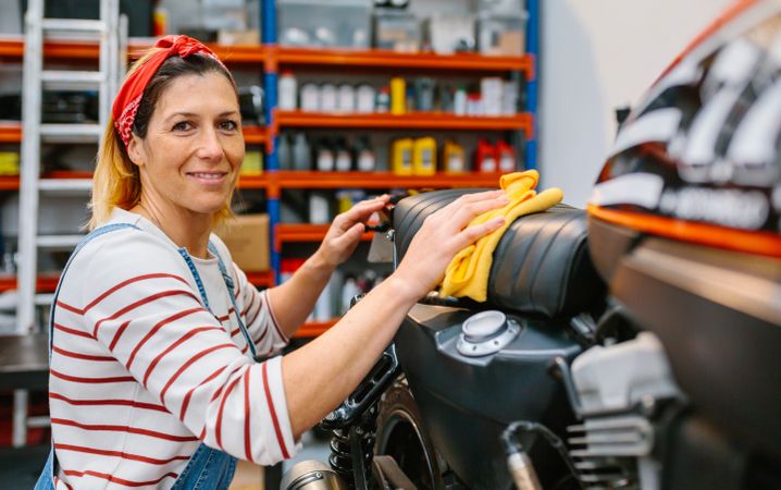 Portrait of smiling female mechanic cleaning motorcycle seat on factory