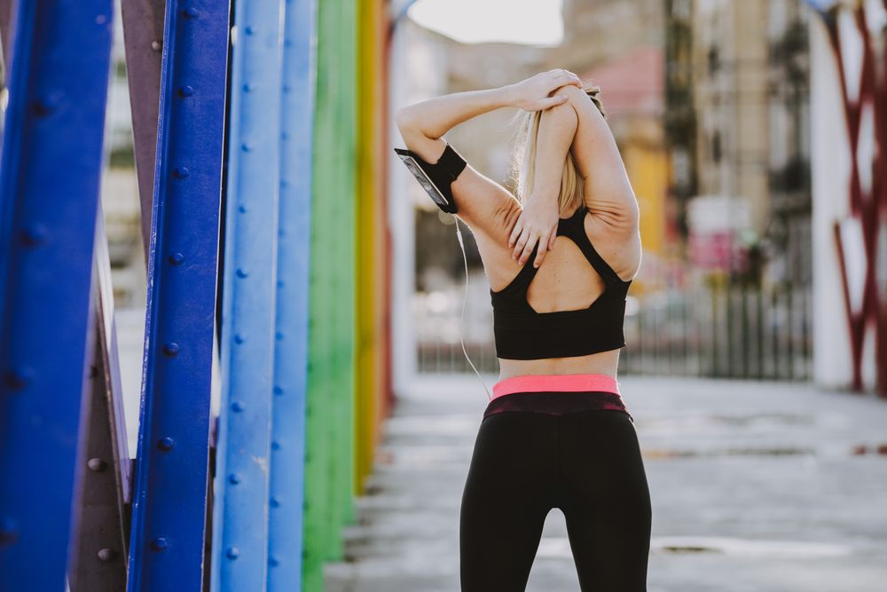 Woman with earphones stretching hands on street