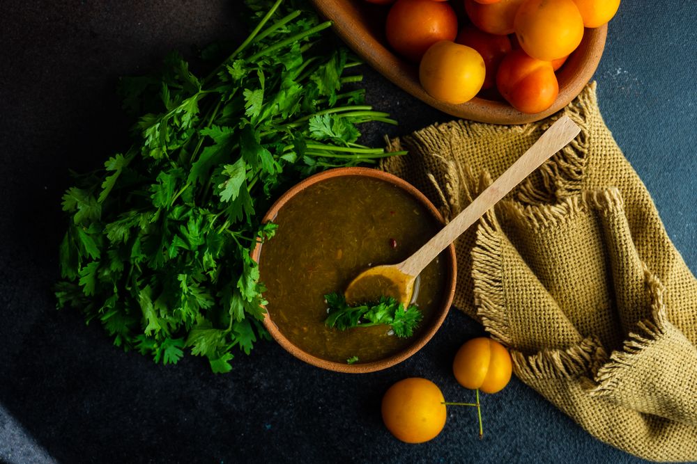 Top view of bowl of plums and fresh parsley with Georgian Tkemali Sauce