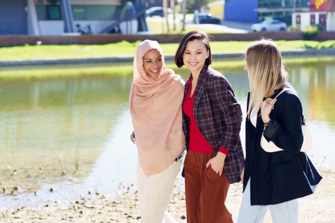 Three women having a conversation while strolling along river bank, copy space