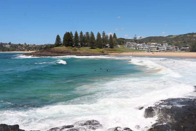 Sunny day at the beach with gentle waves and surfers enjoying the water near residential area