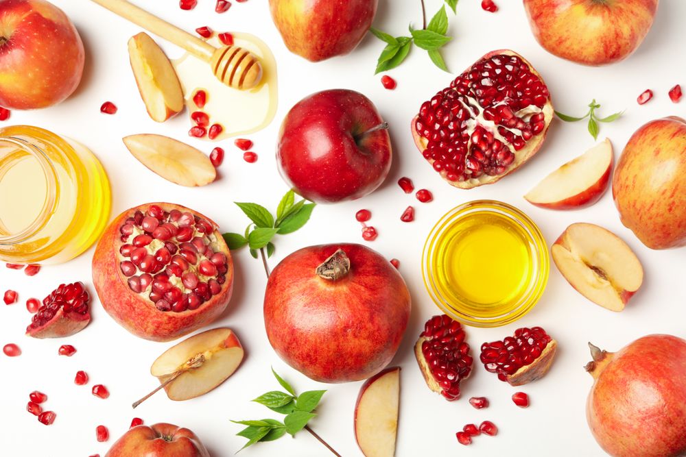 Scattered apples, pomegranates, and honey pot