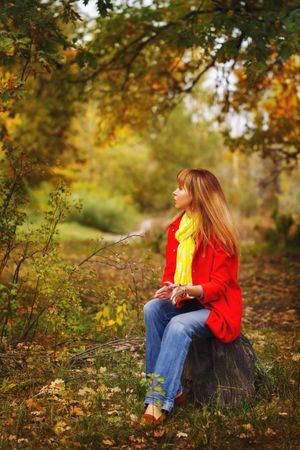 Female in red coat sitting in park surrounded by fall leaves