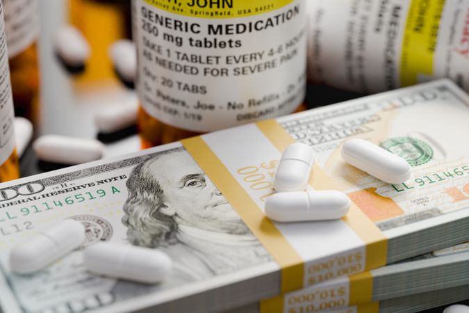 Prescription Medicine Bottles and Pills Next To Stacks of 100 Dollar Bills.