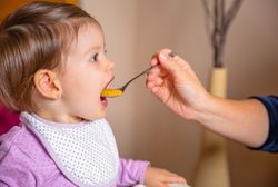 Baby eating puree from a spoon in the hand of mother