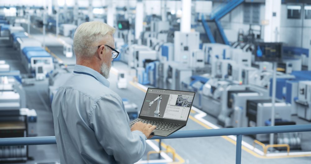 Portrait of an Engineer with Glasses Using Laptop Computer and Looking Around a Factory Facility with Equipment Producing Modern Electronic Components for Different Industries