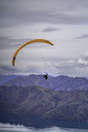 Person paragliding over New Zealand mountains and lake