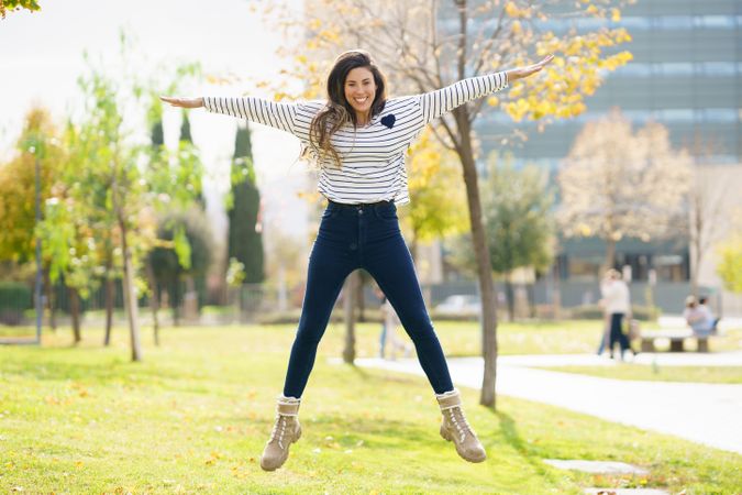 A Joyful Woman is Jumping with Excitement Outdoors in a Beautiful Green Park Setting