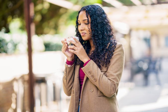 A woman is savoring a warm beverage, such as coffee or tea, while enjoying the outdoors