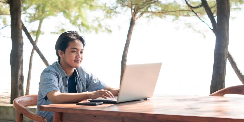 Happy Asian Young businessman work at outdoor with laptop. Concept of remote and freelance work. Young successful man wearing casual blue cloth.