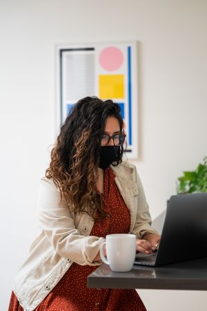 Woman with long curly hair working on a laptop wearing a face mask