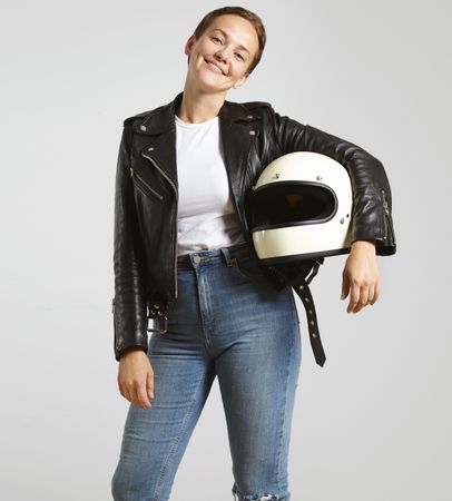 Smiling woman in dark leather jacket with light t-shirt posing with motorcycle helmet under arm