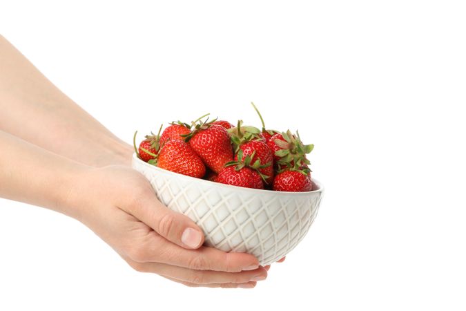 Female hands hold bowl with tasty strawberry, isolated on plain background. Summer berry