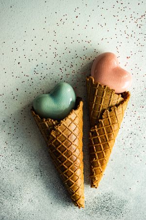 Two ceramic hearts in waffle cones on grey table with glitter
